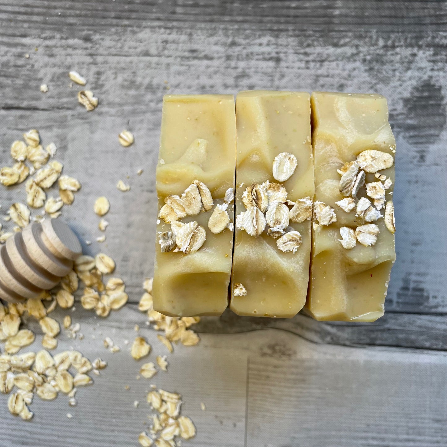 3 honey and oat bars to show the natural color and the texture of the top with Oats as a decorating element. the background shows oats and a honey serving stick