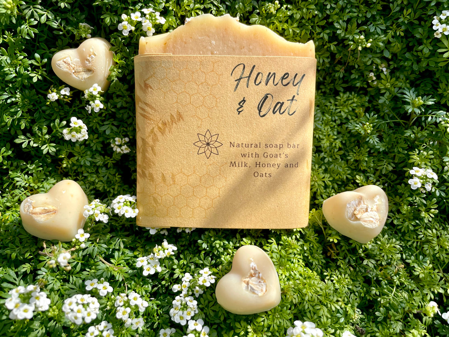 Honey and Oat handcrafted soap, showing the label and front side of the soap to appreciate the size of the bar, it has 4 mini soap samples of the same soap on a heart shape, all on a bed of wild flowers
