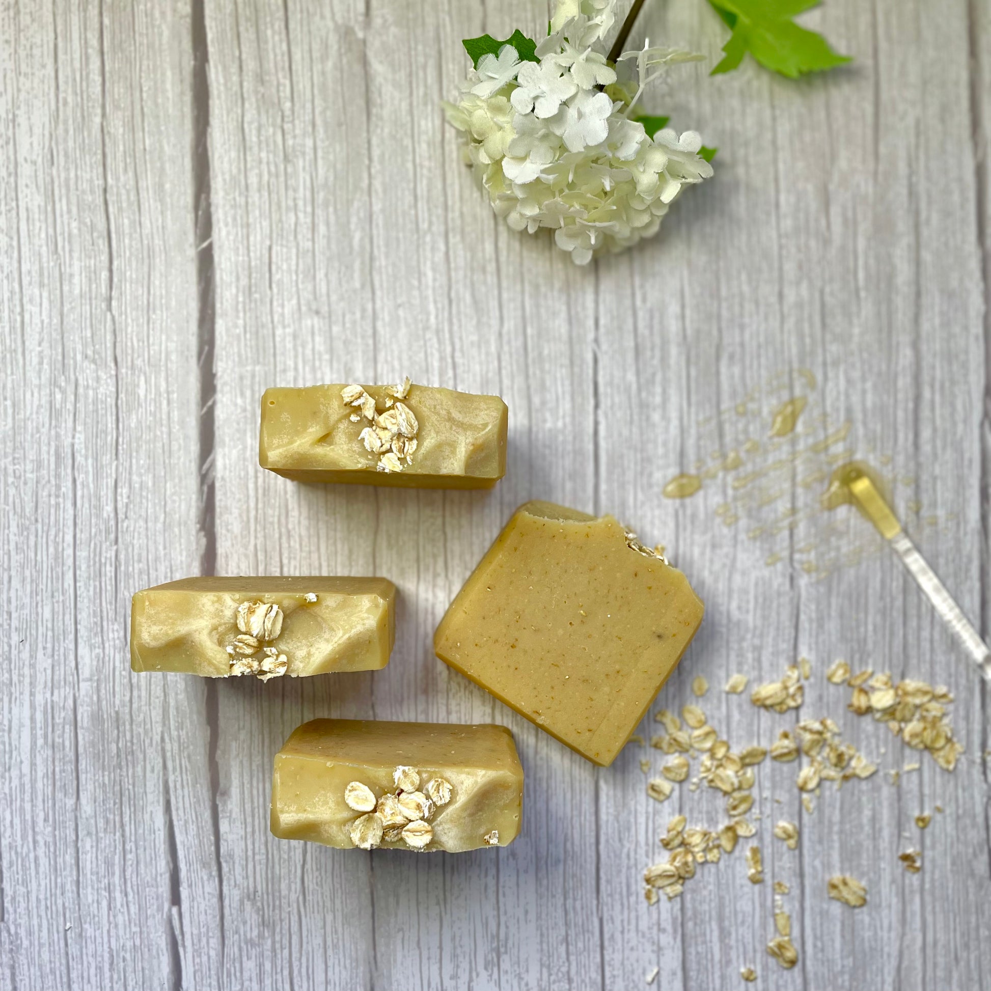 4 honey and oat handcrafted soaps to show the top and front side of the soaps, with some oats and honey as a background with some white flores to make reference of the natural basic clean beauty of this product